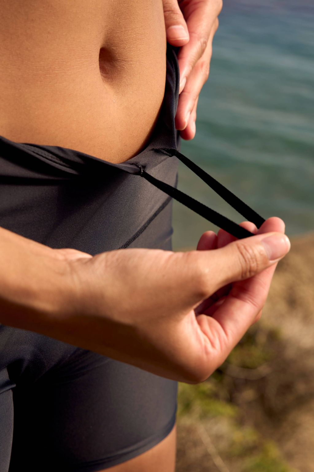 Close-up of a woman wearing the Rysenne Rise Short in Midnight (Black), pulling the adjustable infinity drawcord within the dual-layer waistband to achieve a customized fit.